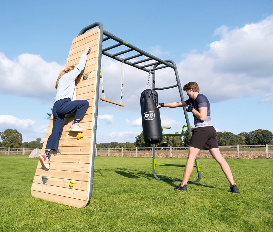 Eine Frau klettert auf das EXIT Klettergerüst MB220, ein Mann boxt gegen einen Boxsack.