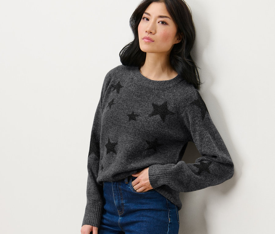 Frau posiert in Strickpullover mit Sternen und Jeans.