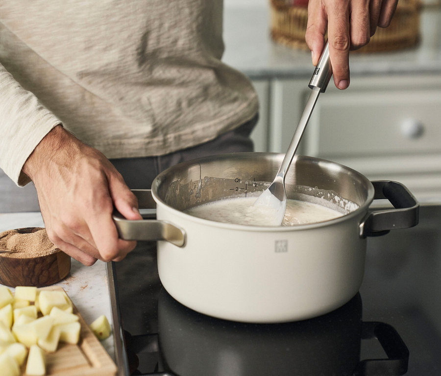 Mann rührt kochendes Essen in einem elfenbeinfarbenen ZWILLING PURE Edelstahl-Kochgeschirr-Set, 5-teilig.