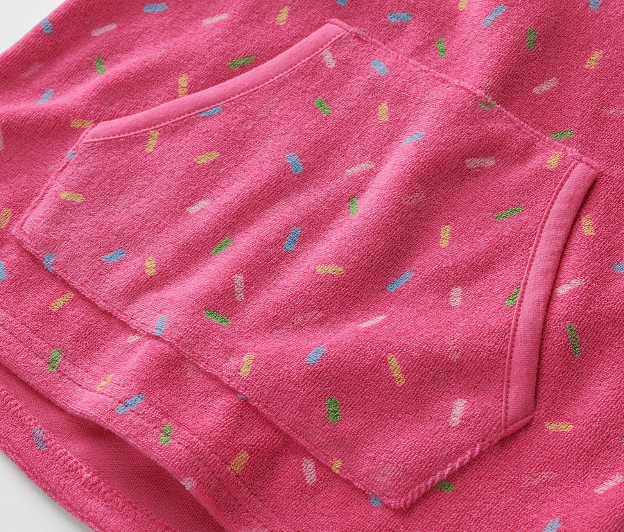 Detailaufnahme eines pinken Kinder-Frottierponchos mit Tasche und bunten Streuseln.