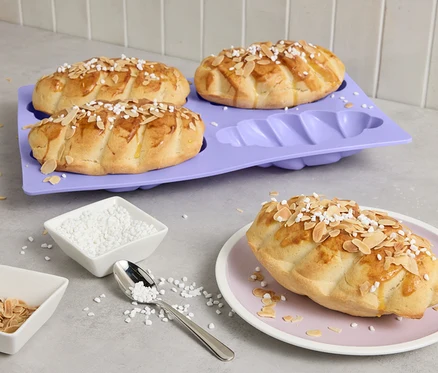 Vier Mini-Hefezöpfe auf lila Backform, einer auf Teller, mit Mandeln und Zucker bestreut.