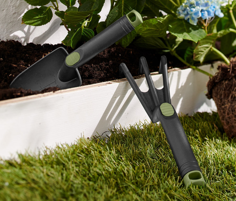 Teil eines Gartenwerkzeug-Sets liegt auf Gras neben einer blauen Hortensie.