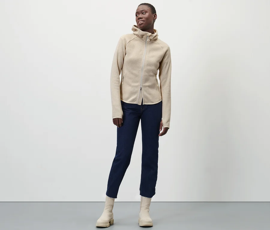 Frau posiert in Strickfleece-Jacke, Jeans und Stiefeln.