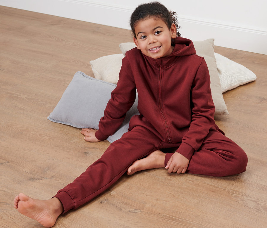 Mädchen sitzt in einem roten Kinder-Lounge-Onesie auf dem Boden.