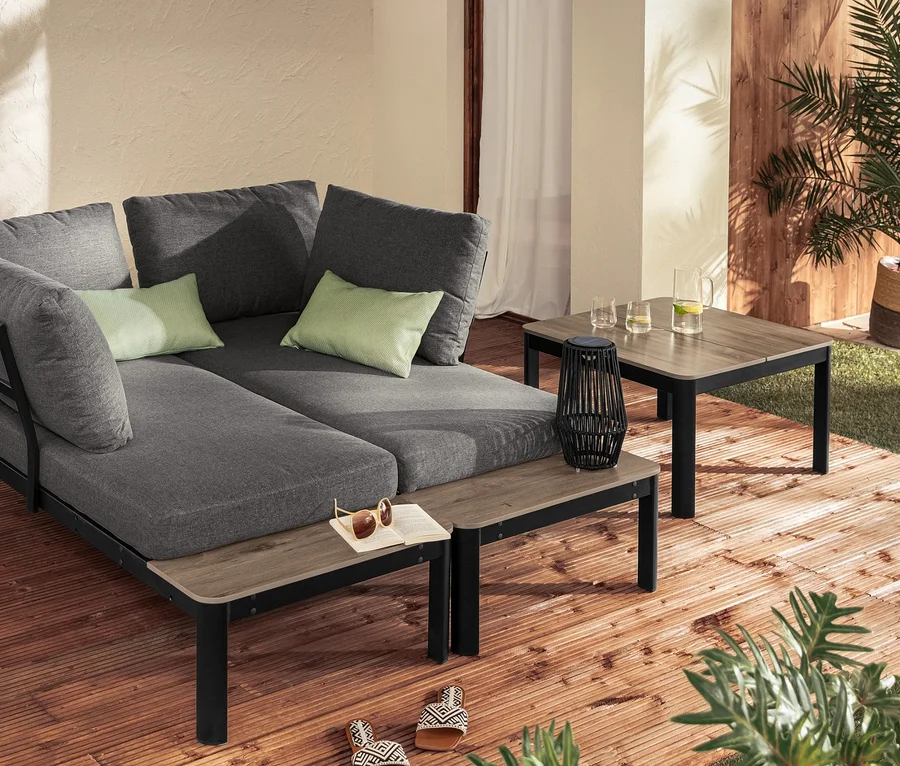 Graue flexible Lounge-Ecke mit Duraboard®-Tischplatten, eine Solar-Laterne und 2 Outdoor-Kissen auf einer Holzterrasse.