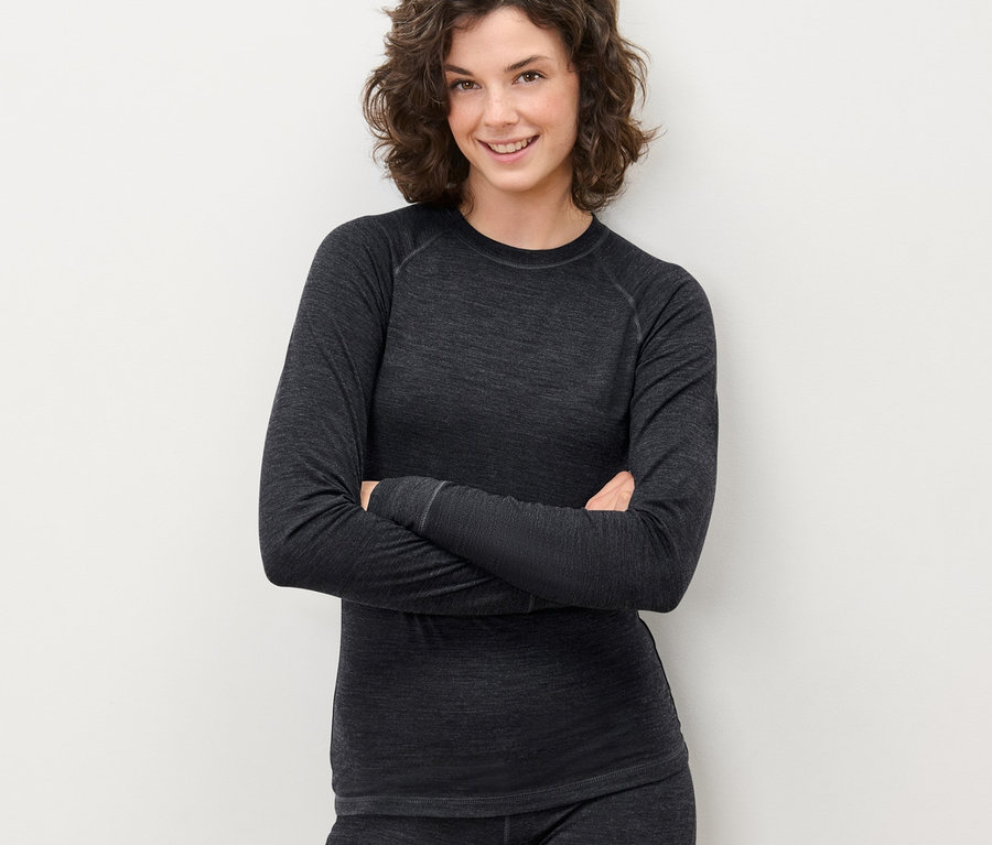 Frau posiert mit verschränkten Armen in einem grauen Funktionsshirt mit RWS-zertifizierter Wolle und Hose.