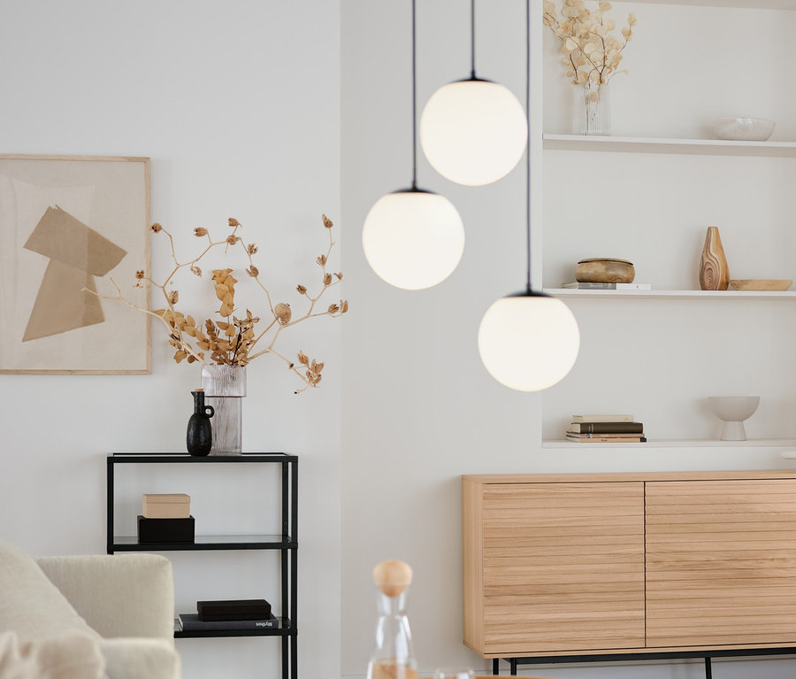 Wohnzimmer mit rundem Couchtisch, Sideboard »Finnsbo« mit Lamellenoptik und Design-Konsole mit Glasfächern. Darüber hängt eine 3-flammige Hängeleuchte mit Glaskugeln.