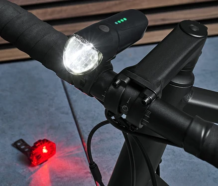 Nahaufnahme eines schwarzen Fahrradlenkers mit eingeschaltetem Vorder- und Rücklicht aus dem Fahrrad-Beleuchtungsset.