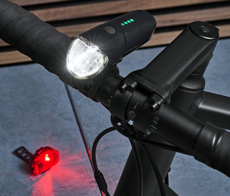 Nahaufnahme eines schwarzen Fahrradlenkers mit eingeschaltetem Vorder- und Rücklicht aus dem Fahrrad-Beleuchtungsset.