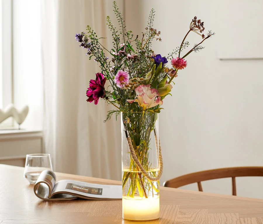 Blumen in LED-Vase auf Holztisch.