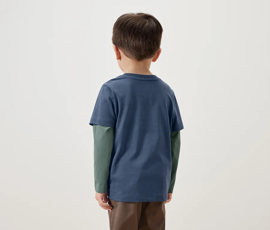 Rückseite eines kleinen Jungen in einem blauen T-Shirt mit langen grünen Ärmeln und braunen Hosen.