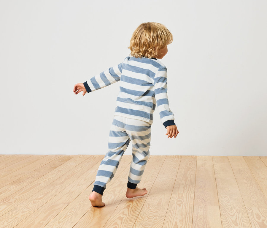 Junge geht in einem gestreiften Pyjama barfuß auf einem Holzboden.