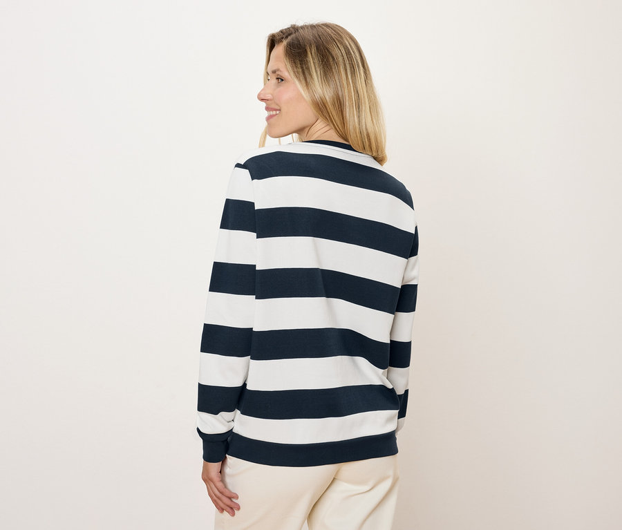 Frau blickt über die Schulter und trägt ein blau-weiß gestreiftes Langarmshirt und eine Hose.