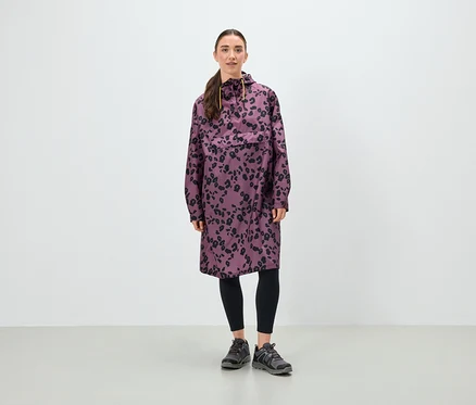 Frau steht und trägt eine lila Tunika mit schwarzem Blumenmuster, schwarze Leggings und graue Schuhe.