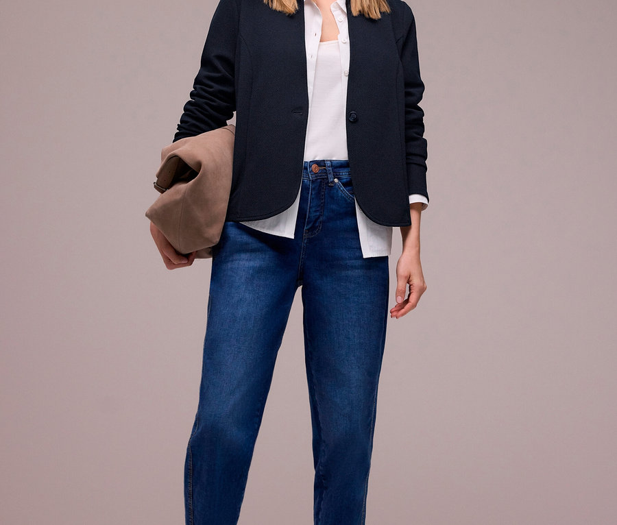 Frau in Jeans und Hemd unter Street One Jerseyblazer. Sie hält eine Tasche und trägt flache Schuhe.