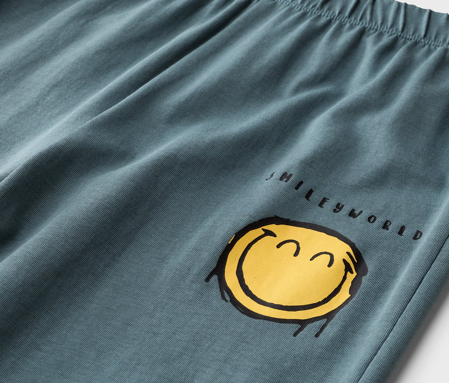 Nahaufnahme einer petrolfarbenen Hose mit Gummibund und gelbem Smileyworld-Aufdruck.