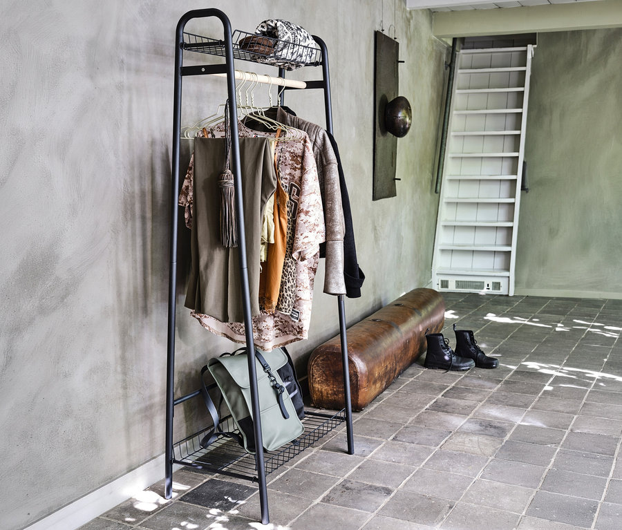 Der schwarze WOOOD Metall-Kleiderständer »Jovi« steht im Raum und hält Kleidung, einen Hut und einen Rucksack.