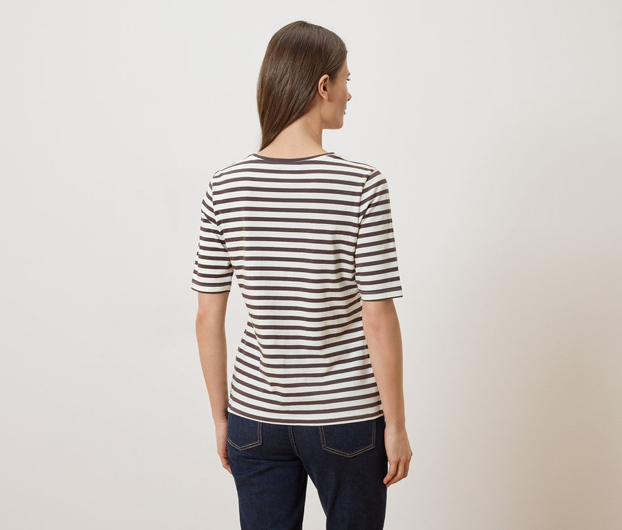 Frau von hinten in gestreiftem T-Shirt und Jeans vor hellem Hintergrund.