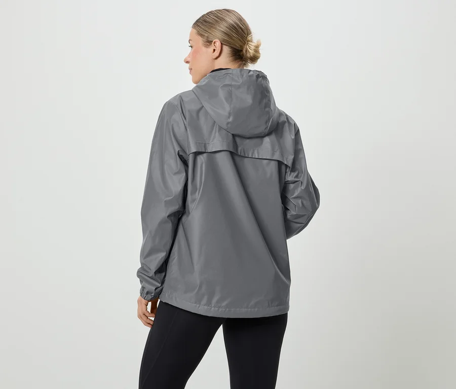Eine Frau mit blonden Haaren trägt eine graue Regenjacke mit Kapuze und schwarze Leggings, von hinten gesehen.
