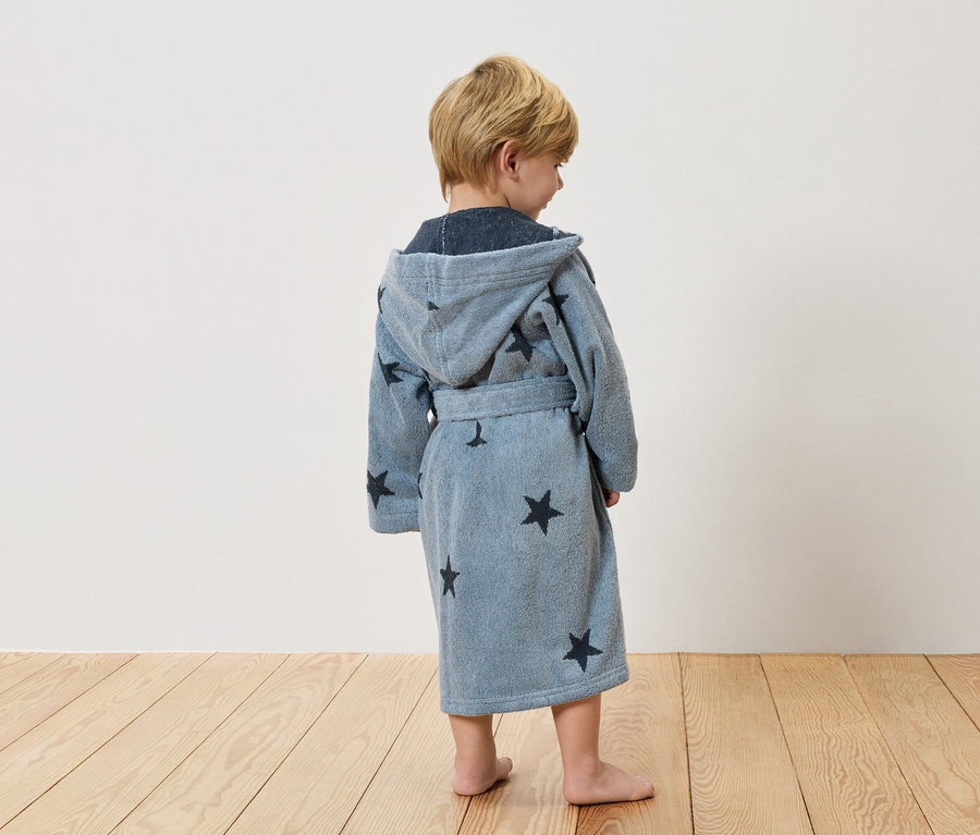 Ein Kind steht mit dem Rücken zur Kamera und trägt einen hellblauen Bademantel mit Sternen.