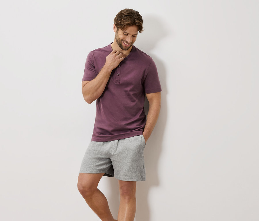 Mann mit weinrotem T-Shirt mit Knöpfen und grauen Shorts.