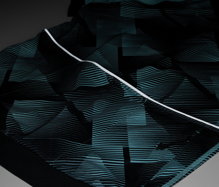 Nahaufnahme eines Kleidungsstücks mit einem sich wiederholenden geometrischen Muster in Schwarz und Türkis, akzentuiert durch einen weißen Streifen.