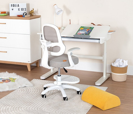 Ein Kinderzimmer mit weißem Schreibtisch, Stuhl, Kommode und Accessoires. Auf dem Schreibtisch liegt ein Buch.