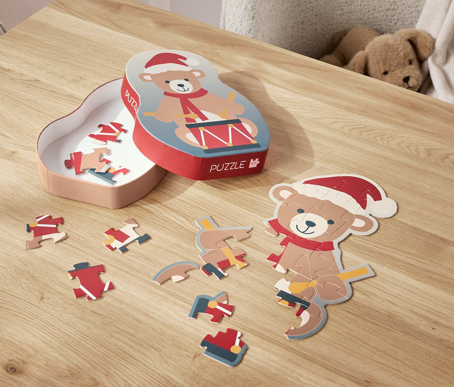 Ein Bär-Puzzle mit Weihnachtsmütze liegt zerlegt auf einem Tisch, daneben die Schachtel.