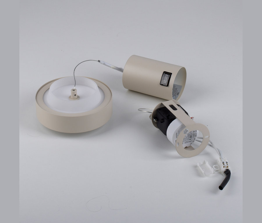 Zerlegte beigefarbene Leuchte auf weißem Hintergrund, bestehend aus einer runden Basis mit Diffusor, einem zylindrischen Gehäuse und einem elektrischen Bauteil mit Kabeln.
