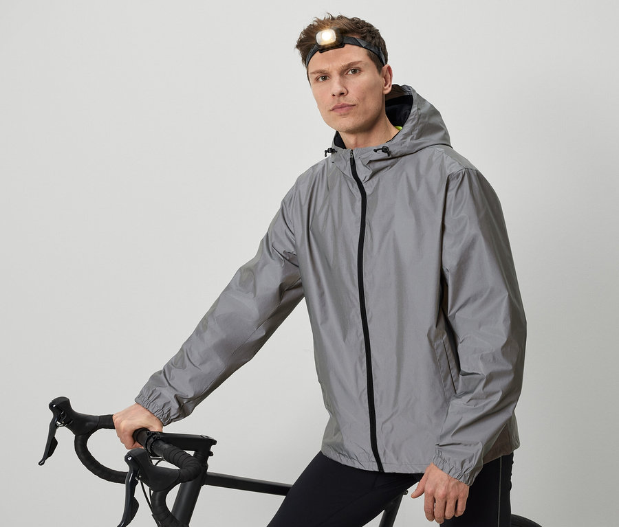 Mann mit Stirnlampe posiert mit Fahrrad in grauer Jacke.