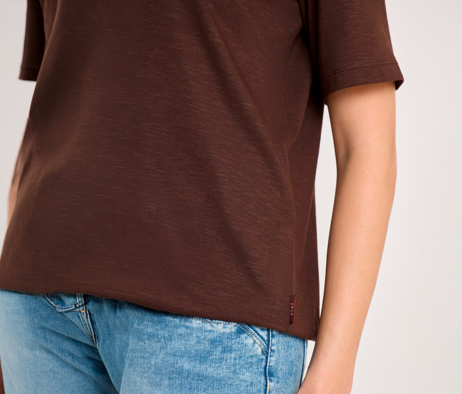 Eine Person trägt ein braunes CECIL Tunika-Shirt mit kurzen Ärmeln und blaue Jeans.