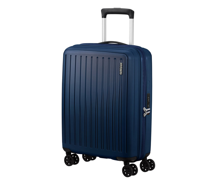 Ein kleiner, navyblauer American Tourister #Rejoy Spinner# Koffer steht aufrecht. Er hat eine geriffelte Oberfläche, einen ausziehbaren Griff, vier Doppelrollen und ein integriertes Zahlenschloss.