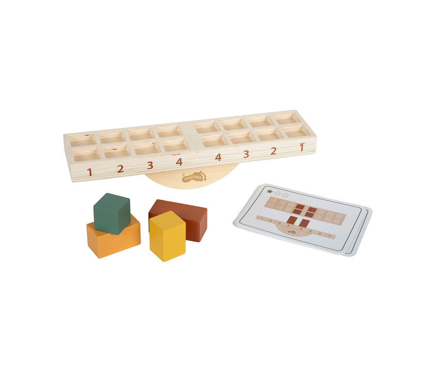 Ein small foot Montessori-Bundle 2, eine hölzerne Waage mit nummerierten Fächern von 1 bis 4 auf jeder Seite, ruht auf einem runden Sockel. Links davon liegen vier bunte Holzklötze (orange, grün, gelb, braun) und rechts eine weiße Musterkarte.