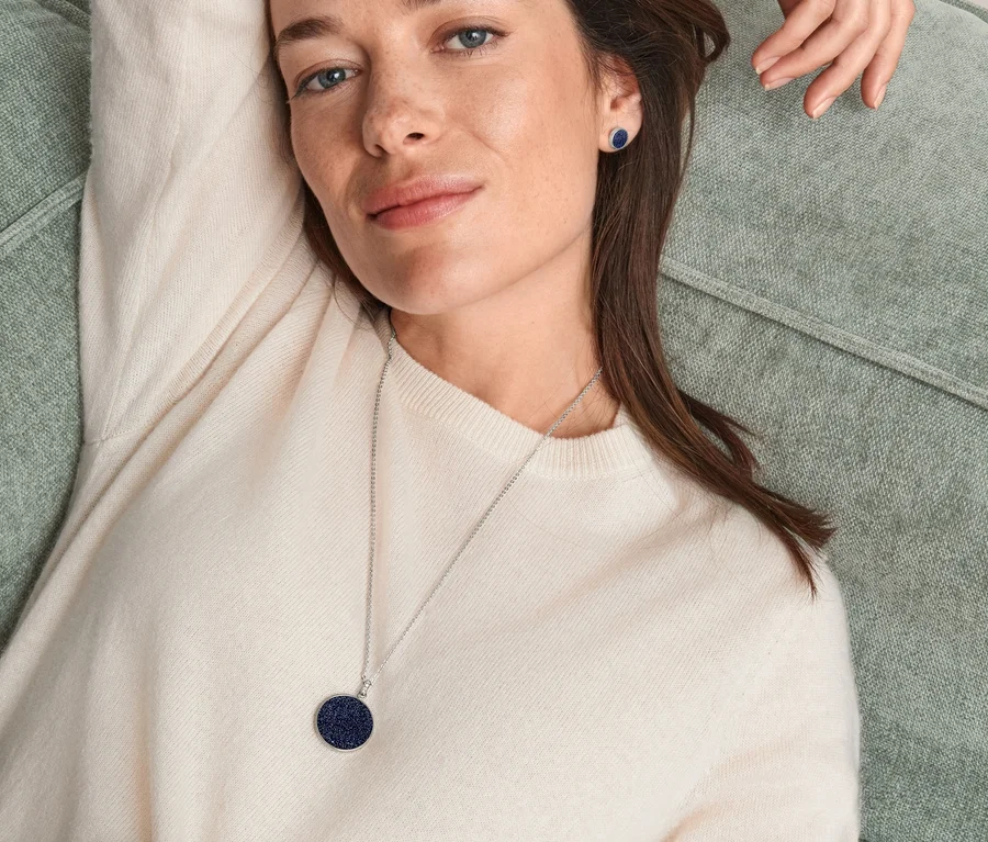 Eine Frau liegt auf einer Couch und trägt einen Ring, Ohrstecker und eine Kette Sternenhimmel.