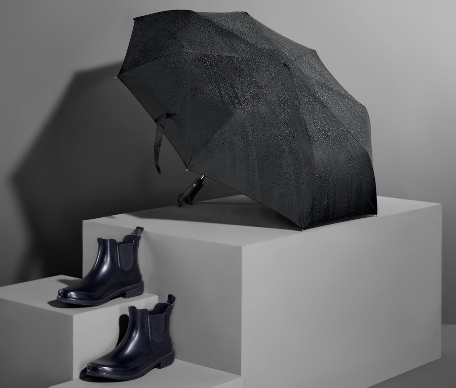 Ein schwarzer Automatik-Taschenschirm und ein Paar schwarze Schuhe auf grauem Hintergrund.
