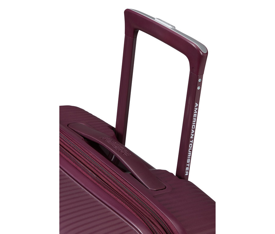 Nahaufnahme eines bordeauxroten American Tourister Koffers mit ausgefahrenem Teleskopgriff. Der Koffer hat eine gerippte Textur, einen weichen Tragegriff und einen Reißverschluss.