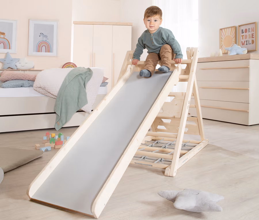 Ein Junge klettert auf ein roba Kletterdreieck mit Rutsche im Kinderzimmer.