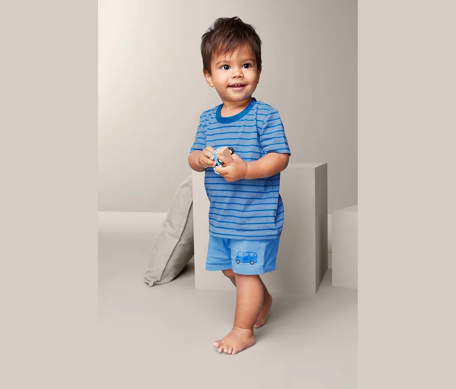 Ein kleiner Junge hält ein Holzspielzeug und trägt ein blau gestreiftes T-Shirt und Shorts mit einem Busaufdruck aus einem 3-teiligen Pyjama-Kombi.