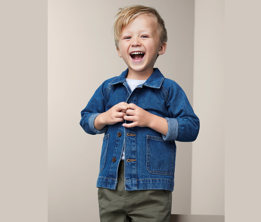 Lachender Junge, der eine Baumwoll-Denim-Jacke zuknöpft.