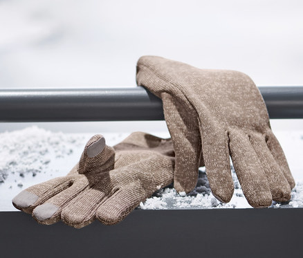 Braune Strickfleece-Handschuhe liegen auf einer verschneiten Oberfläche.