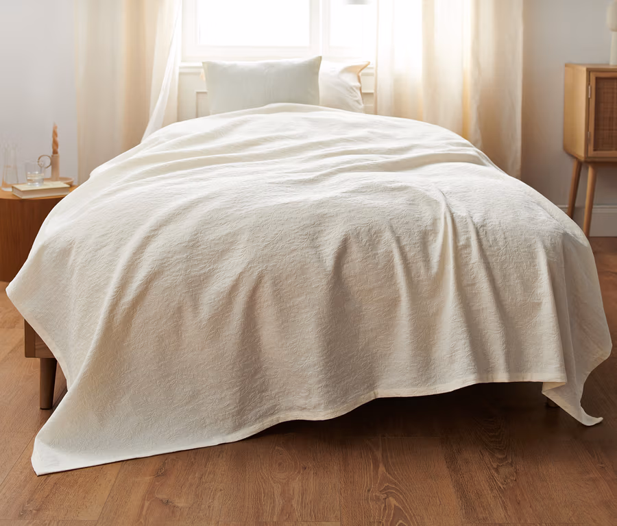 Eine beige Tagesdecke liegt auf einem Bett in einem Schlafzimmer.