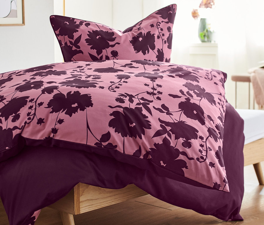 Detailansicht von Premium-Baumwoll-Bettwäsche mit Blumenmuster in Rosa- und Lilatönen auf einem Bett.