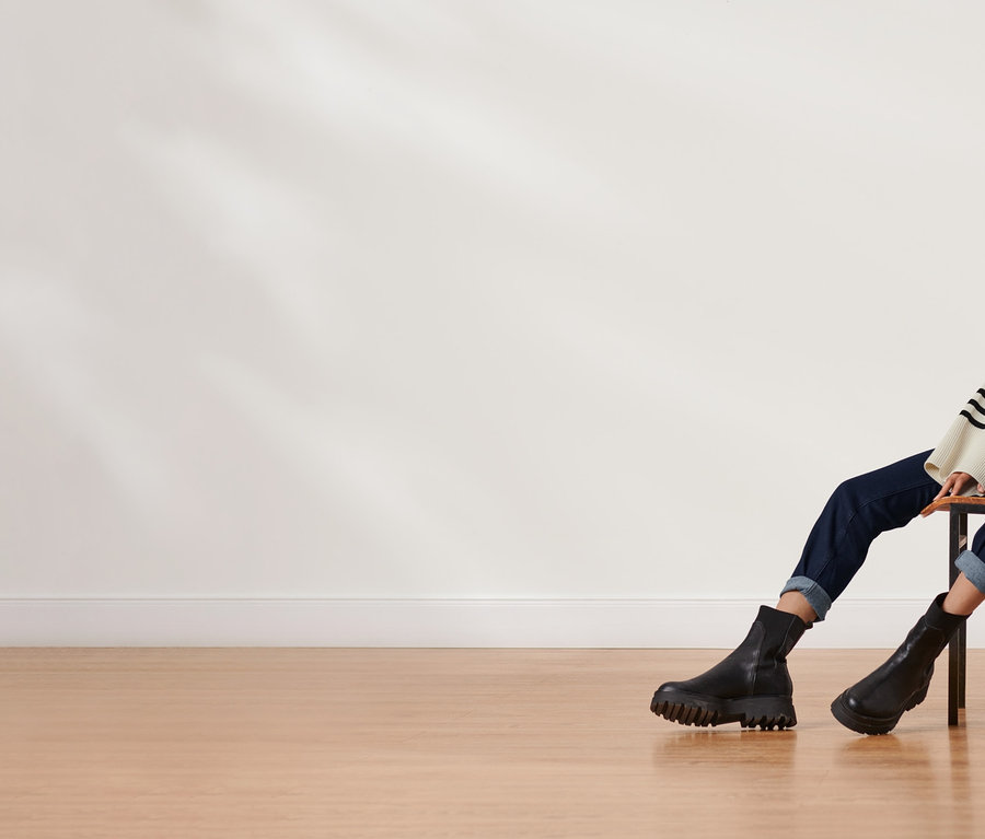 Frau sitzt auf einem Stuhl und trägt einen Strickpullover mit Wolle, Jeans und schwarze Stiefel.