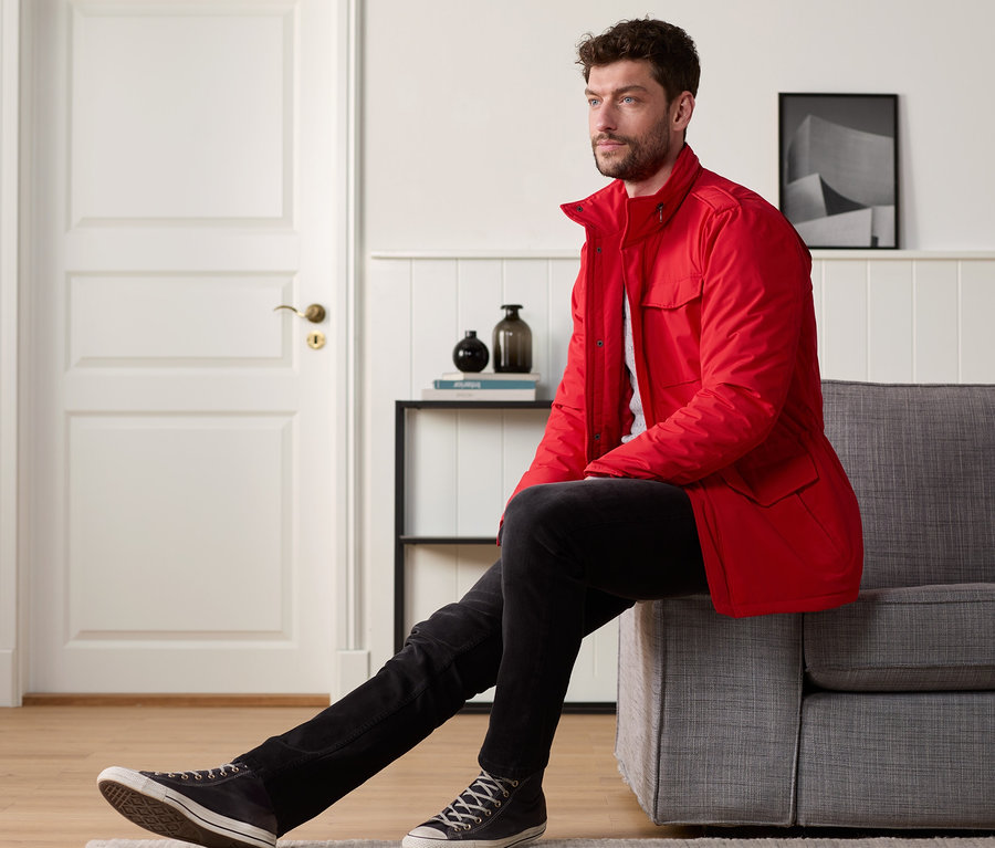 Mann sitzt auf grauem Sofa und trägt eine rote Fieldjacket.