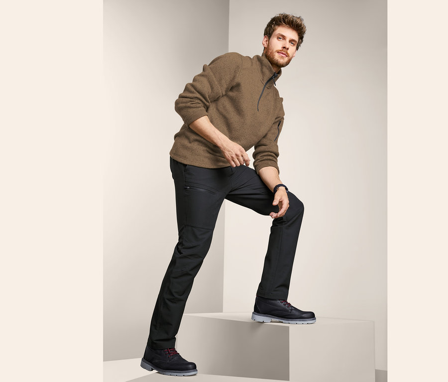 Mann steigt auf weiße Treppe, trägt braunes Sweatshirt und schwarze Outdoor-Thermohose.