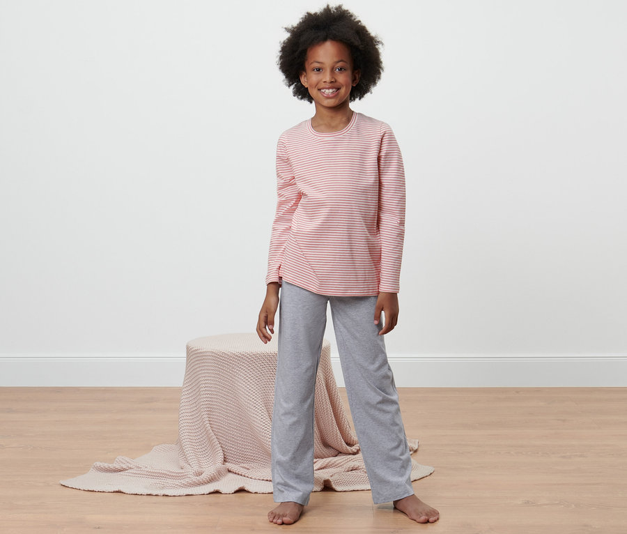 Mädchen trägt 2 Kinder-Pyjamas, gestreiftes, rosa Oberteil und graue Hose.