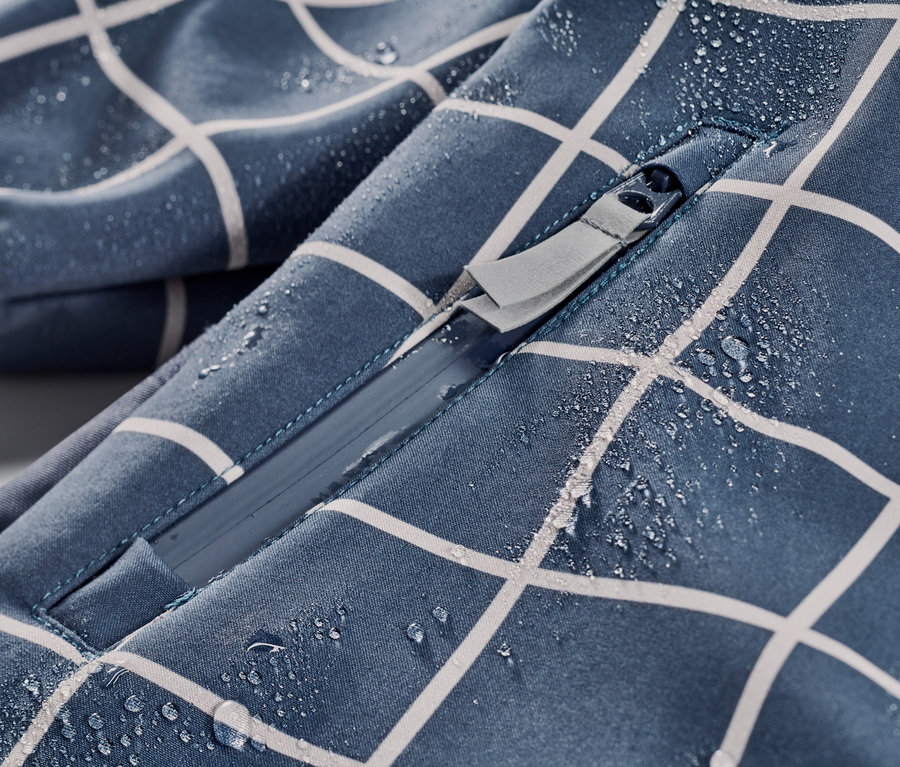 Detailaufnahme eines karierten Kleinkind-Softshell-Einteilers mit Reißverschluss und Wassertropfen.