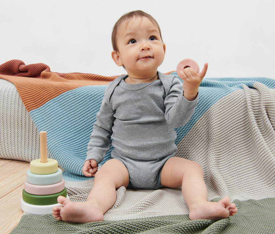 Baby sitzt auf einer Decke und spielt mit Spielzeug, trägt 5 Baby-Langarmbodys.