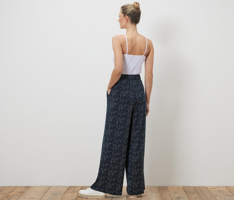 Frau steht mit dem Rücken zur Kamera und trägt eine bedruckte Palazzohose in Dunkelblau-Cremeweiß.