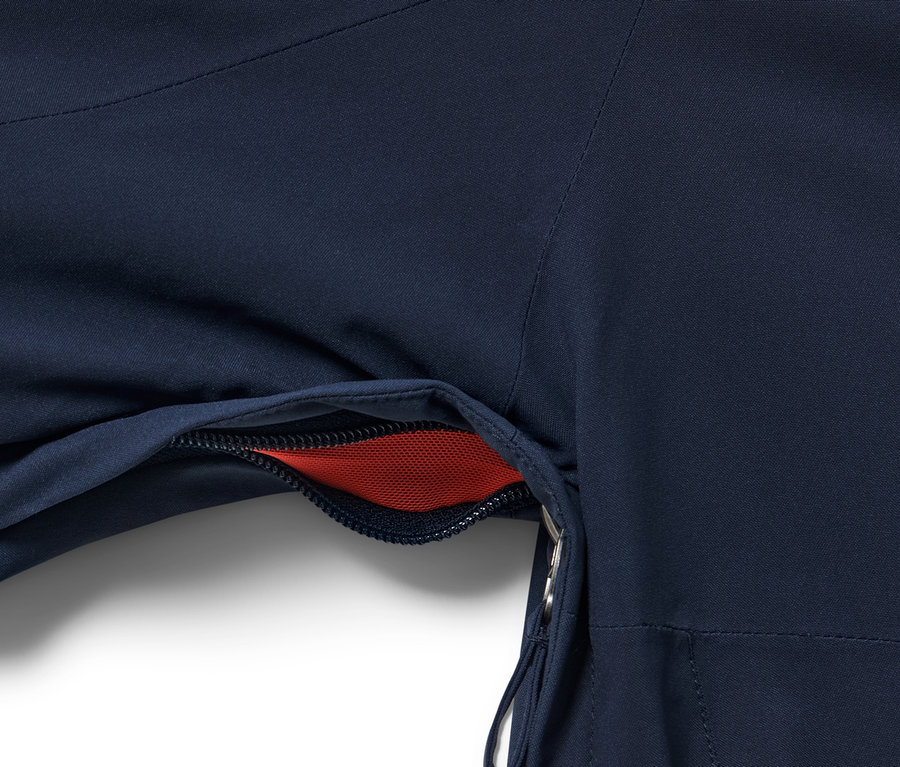 Detailansicht einer blauen High-Tech-Skijacke mit offener Tasche, in der rotes Netzgewebe sichtbar ist.
